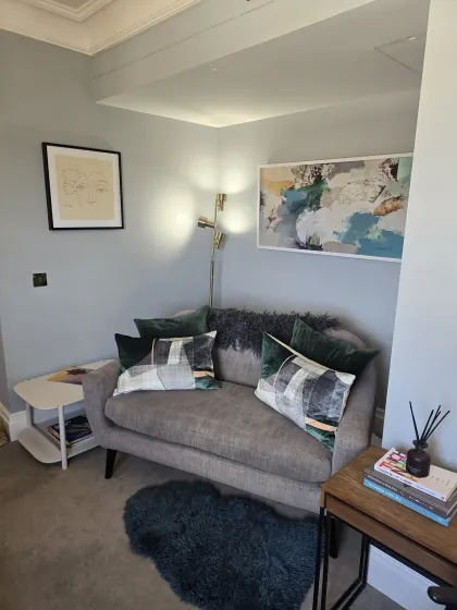 A quiet seating area at Eaton Gate Practice with a sofa, side table, books, and wall art